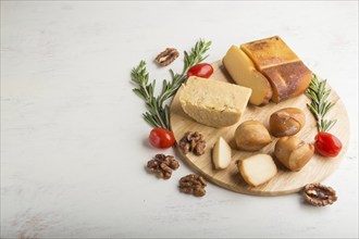 Smoked cheese and various types of cheese with rosemary and tomatoes on wooden board on a white