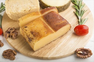 Smoked cheese and various types of cheese with rosemary and tomatoes on wooden board on a white