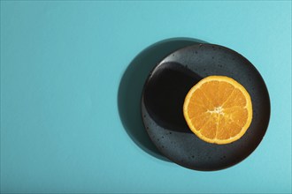 Ripe cut orange on blue ceramic plate on blue pastel background. Top view, flat lay, copy space,