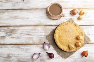 Autumn onion pie and cup of coffee on white wooden background and linen textile. Top view, flat