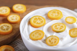 Greek yogurt with kumquat pieces in a white plate on a brown wooden background, close up