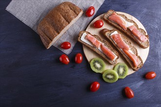 Smoked salmon sandwiches with butter on dark wooden background. cherry tomatoes. top view, copy