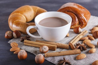 A cup of hot chocolate with nuts, buns and spices on linen napkin and black wooden background.