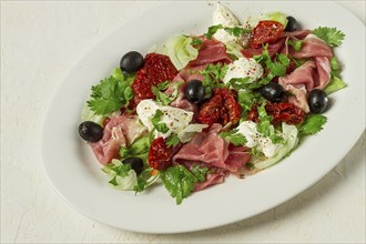 Salad with dried tomatoes, prosciutto, soft cheese, olives, homemade, top view