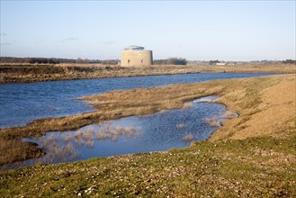 Martello tower standing by coastal defence embankment and lagoon of water, Alderton, Suffolk,