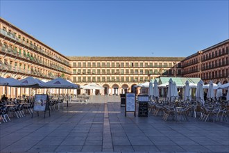 Large plaza with arcades, full of café tables and umbrellas, evening atmosphere with a convivial