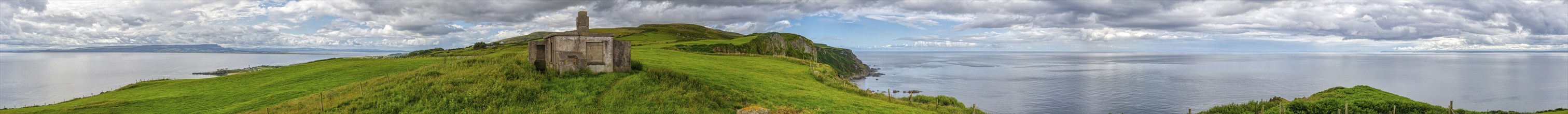 A lonely lighthouse on a green hill overlooking the sea under a cloudy sky, Inishowen Head