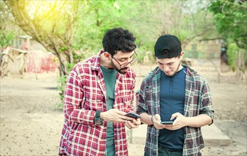 Two teenage guys pointing and checking their cell phones, Two friends looking at the content of