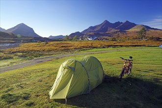 A tent and a bicycle stand on a green meadow with mountains in the background, ideal for camping,