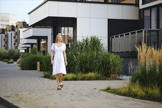 Young woman in sundress walking along the pavement in modern residential area