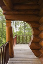 Brown reddish stained Scandinavian log cabin home with arch and wall made of large chinked logs and