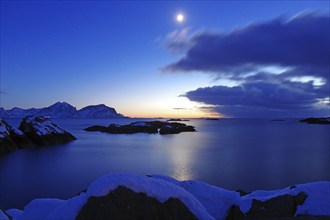 Winter coastal landscape at dusk with snow-covered islands, clear sky and moon, Nyksund, Langoya,