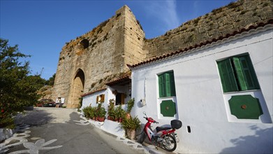 A white house with green shutters next to an ancient wall under a clear sky, Koroni, Byzantine