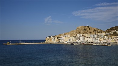 Coastal town by the sea with white buildings, hills in the background and boats in the harbour