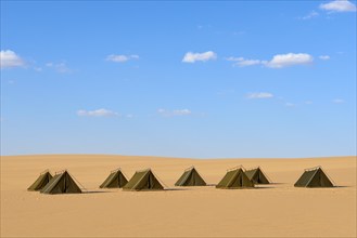 Row of tents in a sandy desert landscape under a blue sky with few clouds, Matruh, Great Sand Sea,