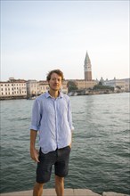 Young man in striped shirt and shorts on the banks of the Grand Canal, behind Campanile, Venice,