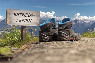 Symbolic image of company holidays/summer holidays: Hiking boots in front of an alpine backdrop and