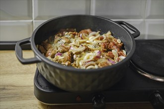 Beef and vegetables ragout is cooked on portable electric stove in the kitchen