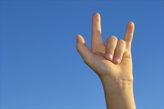 A child's hand gestures against a clear blue sky, symbolic and expressive