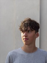 Portrait of a young athletic man with curly brown hair in front of a grey wall, looking into the