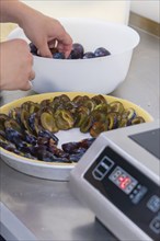 Person arranges plum halves on the pastry base of a cake