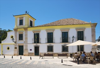 Colonial-style building with yellow accents, outdoor seating under parasols, Consulado-Geral do