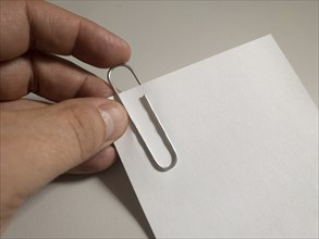 A hand attaches a paper clip to a piece of white paper