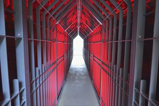 A long tunnel with red lighting and metallic structures conveys a futuristic and industrial