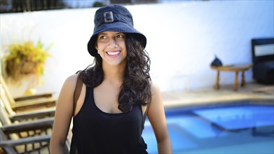 Portrait of pretty girl with hat smiling near a swimming pool. latin girl smiling with swimming