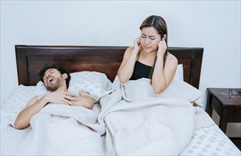 Husband snoring while the wife suffers and covers her ears. Sleep apnea concept, Snoring man in