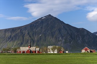 The small village of Flakstad with its red church and a few houses, with Mount Hustinden in the