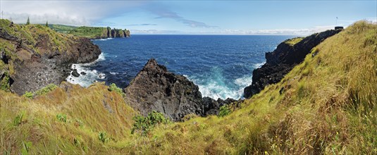 Panorama of a rocky coastal view with rugged cliffs plunging into the blue sea under a clear sky,