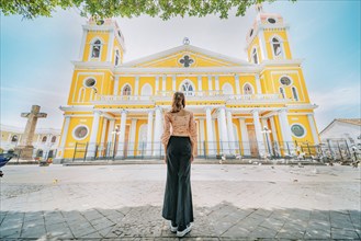 Rear view of a tourist woman in front of a cathedral in a tourist square. Back view of a beautiful