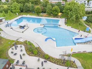 Aerial view of an outdoor pool with swimming pool, deckchairs and tables, surrounded by trees and