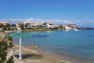 A quiet beach with clear water and houses on the shore under a blue sky, Archangelos, Mani,