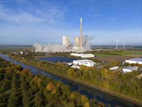 A coal-fired power station with smoking chimneys in a rural setting, surrounded by wind turbines