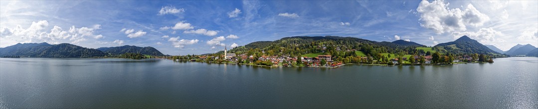 Painter's panoramic view of a Bavarian village on a lake, surrounded by mountains under a blue sky