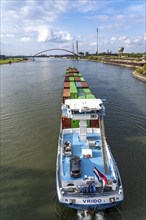 The Dutch cargo ship Vrido, loaded with containers, on the Rhine near Duisburg, descending, behind