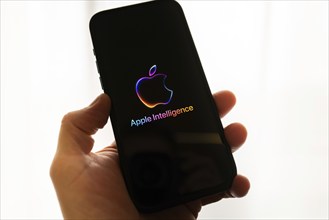 Hand holding iPhone with Apple logo and the text 'Apple Intelligence', bright and modern