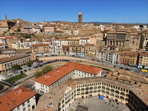 Aerial view of a historic city with many tiled roofs and a striking tower in the centre, aerial