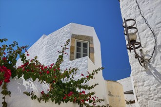 White building with flower tendrils and windows under a bright blue sky, Chora, Old Town, Patmos,