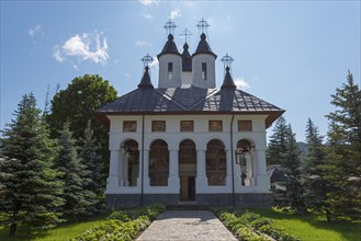 Exterior view of an Orthodox church with white walls and black domes under a clear blue sky, Cheia