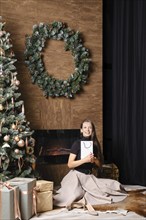 Happy woman sitting on the floor by the fireplace hugging a gift in her hands