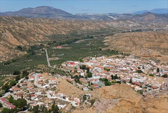 A small village with orange-coloured roofs is nestled in a green valley surrounded by mountains