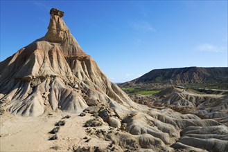 View of a rock formation in a dry, barren desert landscape. In the background, other hills rise up