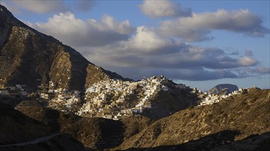 A picturesque village in the mountains, illuminated by sunbeams, surrounded by dramatic clouds,