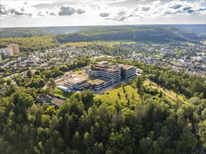 Expansive forest and urban landscape with a large building in the centre, under a cloudy sky,