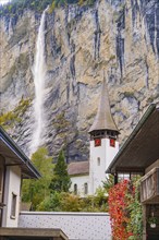 Church tower in front of a dramatic waterfall and rock face in an autumn landscape, Lauterbrunnen,