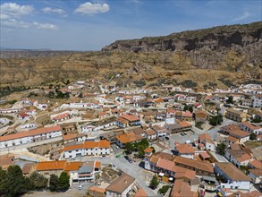 Small village with white houses and red roofs in a rocky hilly landscape under a blue sky, aerial