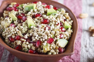 Salad of germinated buckwheat, avocado, walnut and pomegranate seeds in clay plate on white wooden